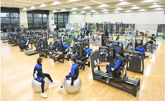 沢山のトレーニングマシンが設置されている広い室内で学生たちがトレーニングをしている様子