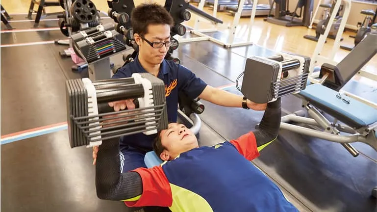 トレーニングマシンを使用している男性と、サポートをしている男性の様子