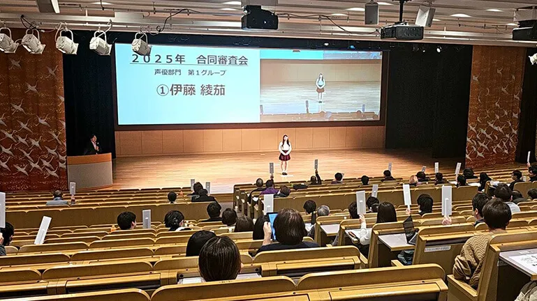 舞台上に立つ学生と観客席で白い札を挙げているたくさんの観衆の様子