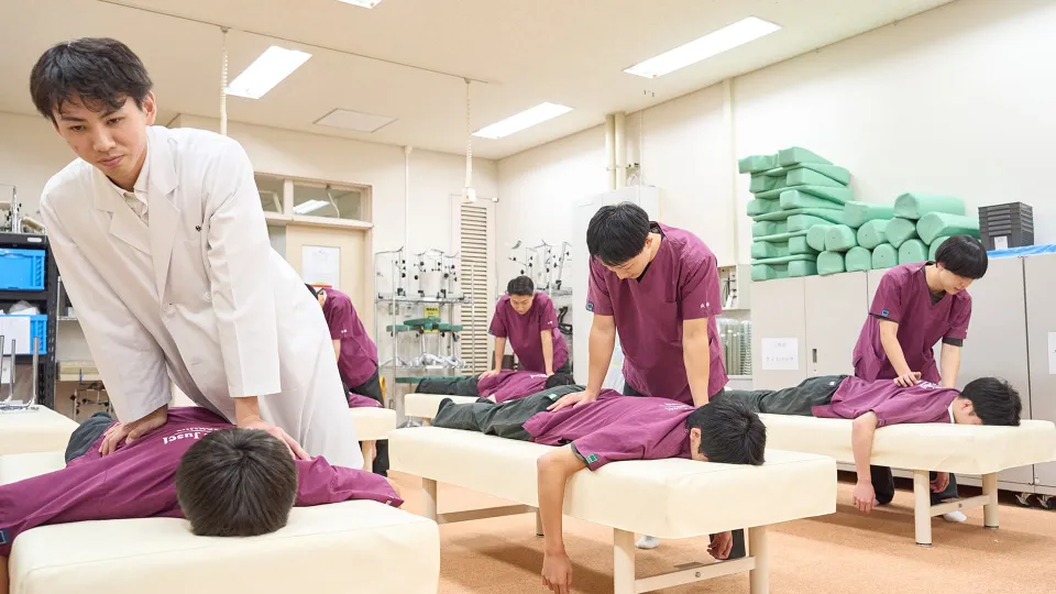 学生たちが講師とならんでベッドに横たわる人に施術をしている様子