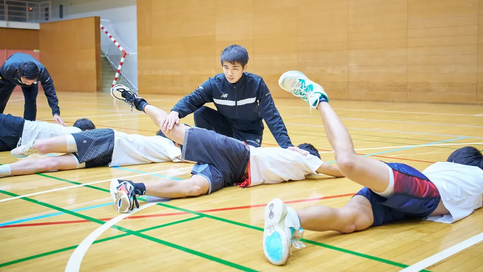 体育館の床に寝そべってのトレーニングをサポートしている様子