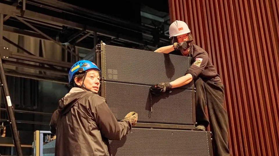 学生たちがヘルメットを着用し音響機器の設置作業を行っている様子