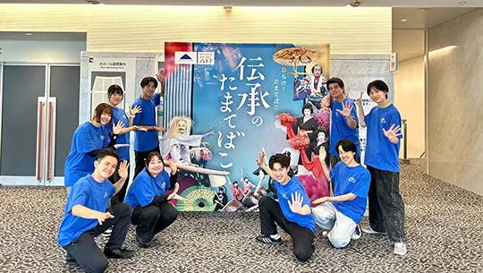 「伝承のたまてばこ」の看板と一緒に記念撮影をする学生たち