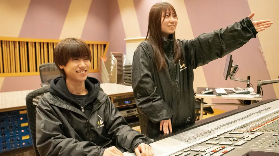 バンドに録音開始のサインを送る学生2人