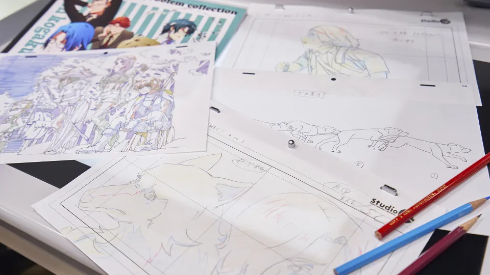 アニメーション用に描かれた、たくさんの作画と、色鉛筆が置かれた机の上。