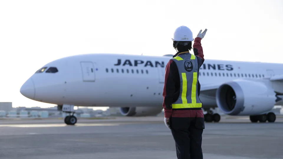 空港のJAL便に手を振るグランドハンドリングスタッフ
