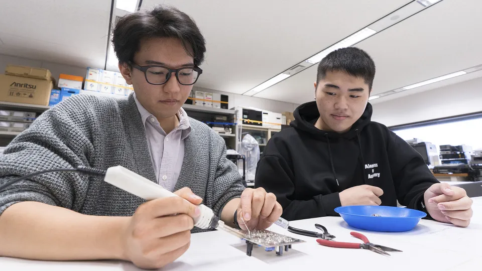 ハンダごてを使って電子工作をする学生とそれを見学する学生