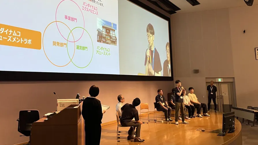 産学連携プロジェクトについて壇上で学生に向けて説明するバンダイナムコアミューズメントラボ開発担当者