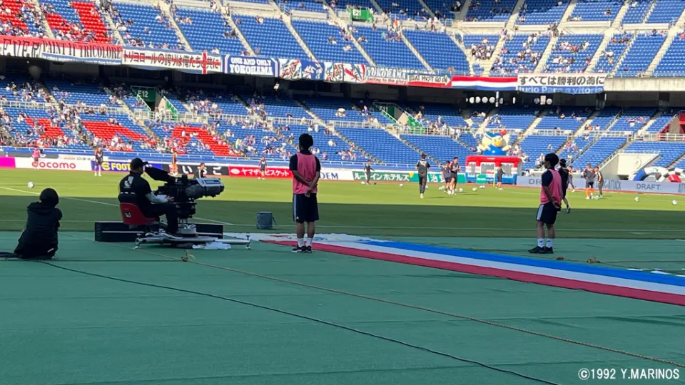 日産スタジアムのピッチサイドでボールパーソンとして待機するサッカーコースの在校生