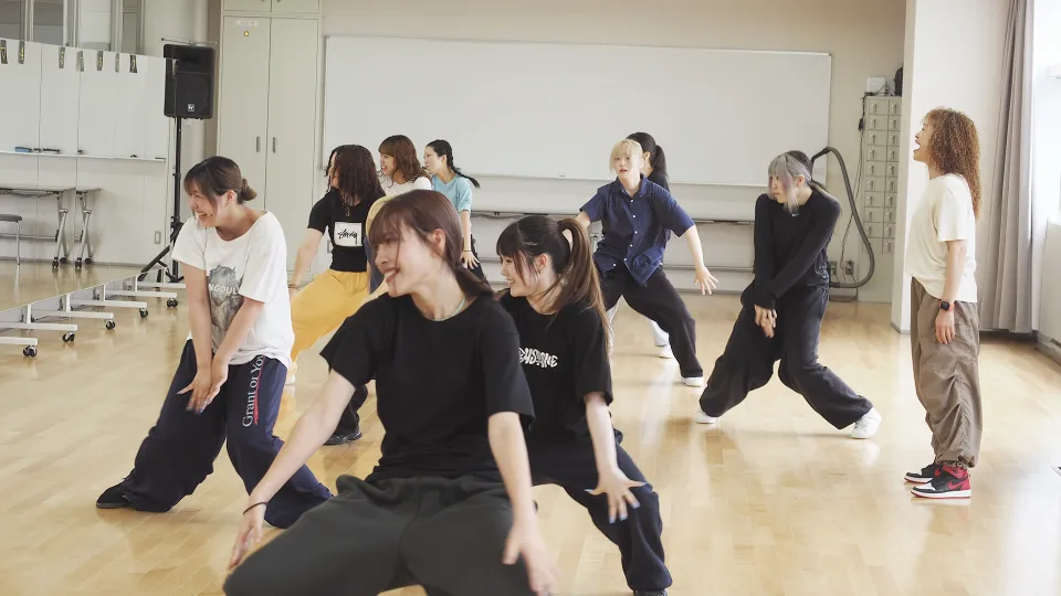 ダンススタジオで鏡越しの笑顔で踊る学生たちと指導する先生