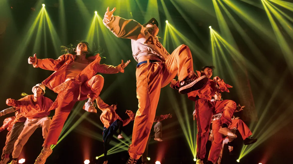 照明を浴びながらステージで踊る、オレンジの衣装のダンサーたち