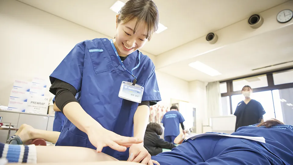 横たわる学生のふくらはぎに針を打つ笑顔の学生