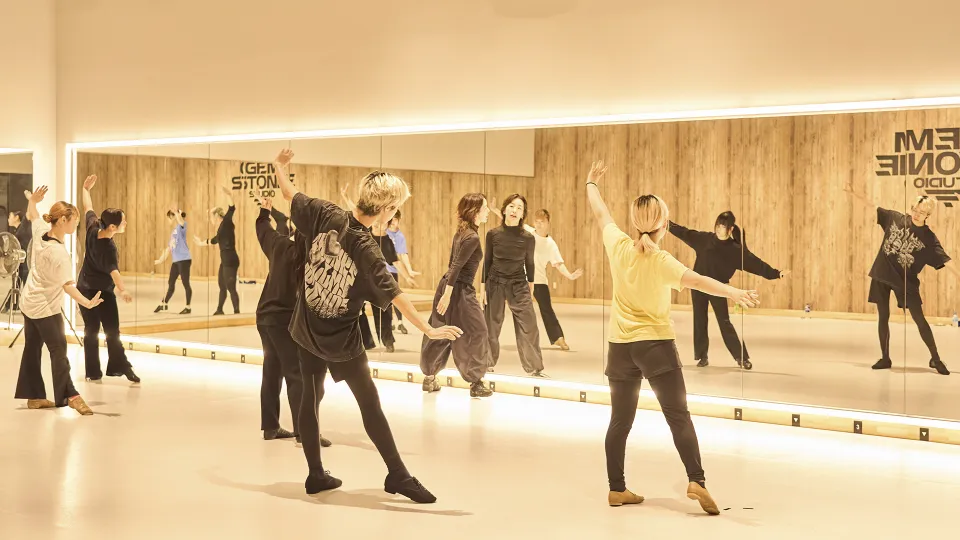 明るいダンススタジオで鏡越しにダンスの指導をうける学生たち