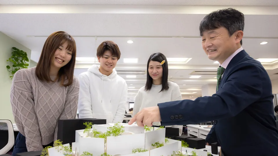 建築の立体模型で説明する先生と笑顔で聞く学生たち