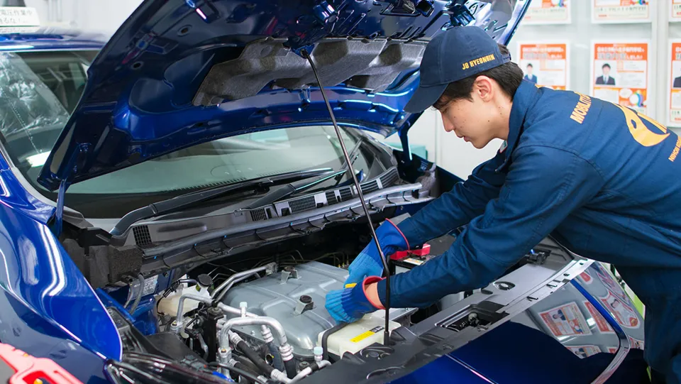 自動車のボンネットを開けエンジンの点検をする学生