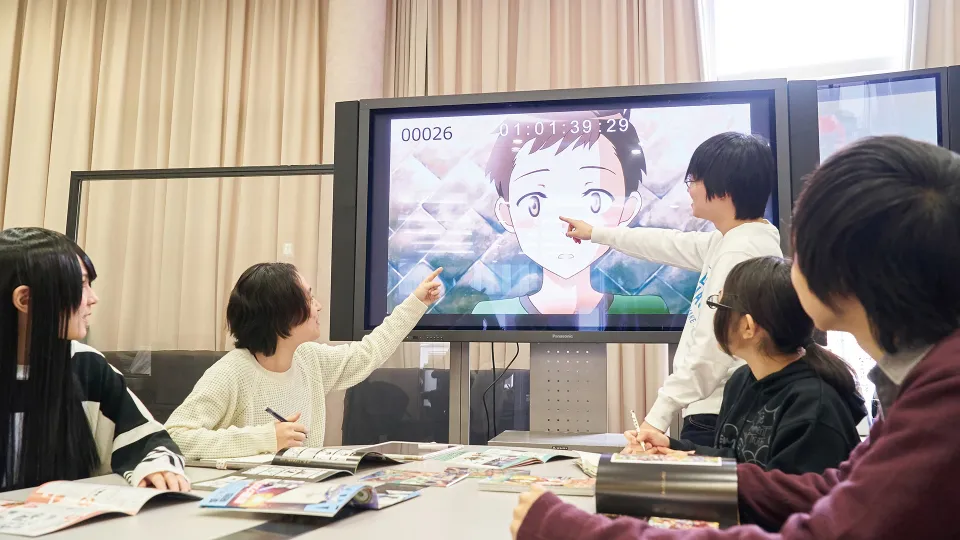 モニターに映されたアニメキャラクターについてディスカッションする学生たち
