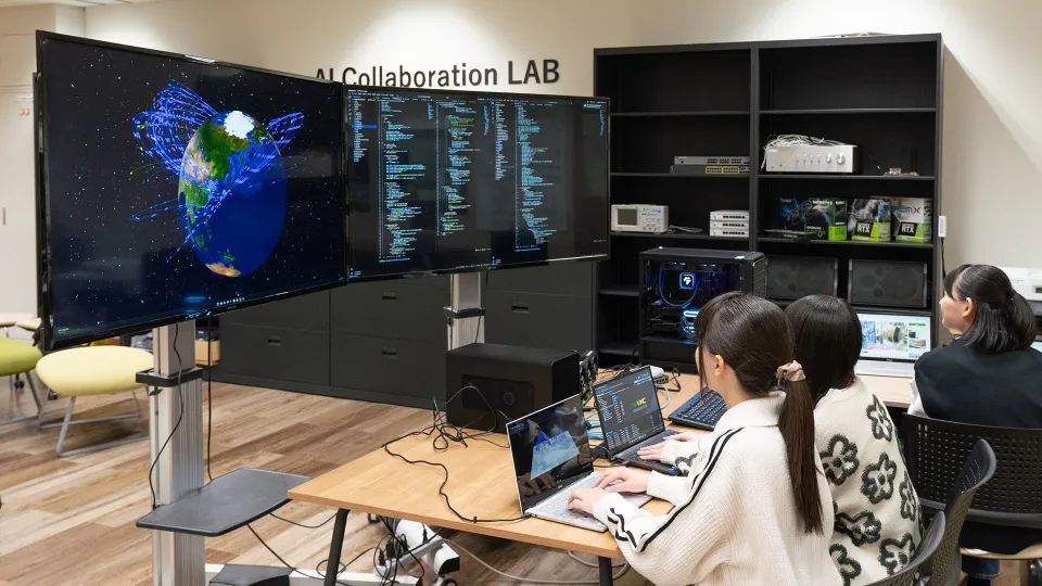 大型モニターに地球の3D映像とコードを映しながら作業する学生たち