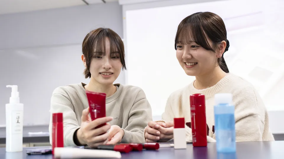 化粧品を並べたテーブルの前で笑顔を会話する2人の学生