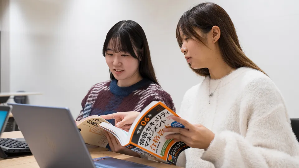 CCNAの参考書を見ながら一緒に勉強する二人の学生