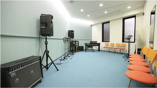 複数のスピーカー、ミキサー、キーボード、アンプ、椅子が完備されたスタジオ