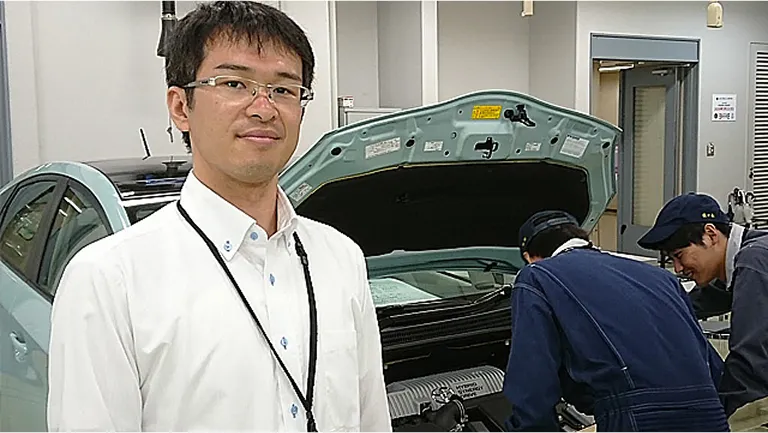 正面を向いている圷 裕光先生と後ろで自動車の整備をしている学生たちの様子