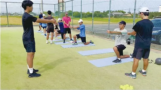 学生たちがテニスコート外で指導を受けている様子