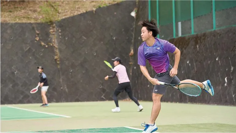 ラケットを振り切っている学生と、ラケットを構えている学生2人の様子