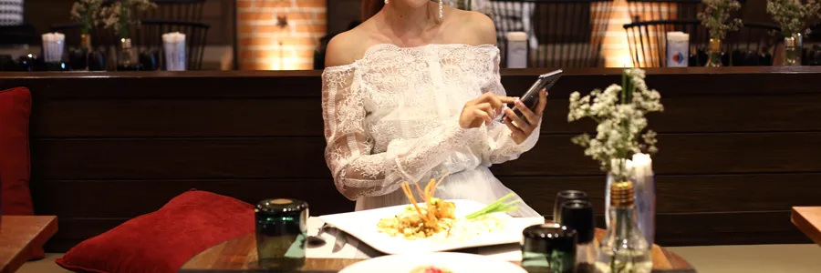 ドレスを着たお客様がレストランでスマートフォンを使用するイメージ画像