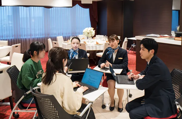 実習ユニフォームを着たホテル観光コースの学生たちから聞き取りを行うAIシステム科の生徒達