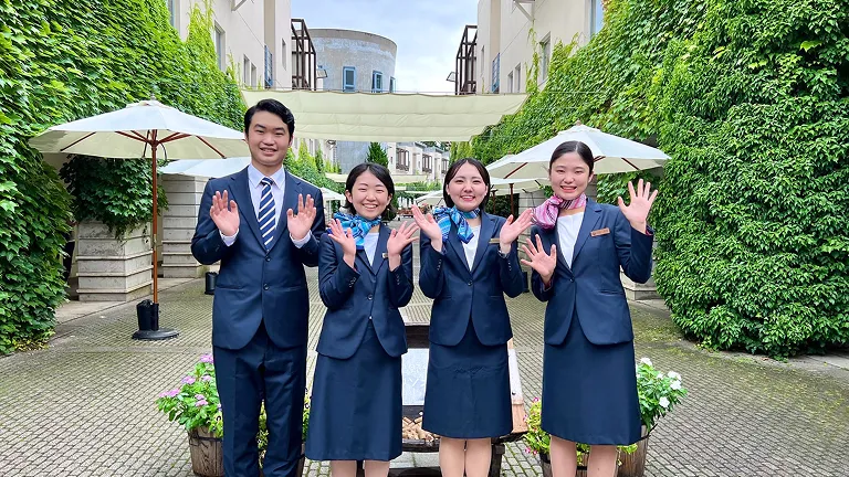 インターン先のホテルサービス担当の制服を着た生徒達が笑顔で手を振っている画像