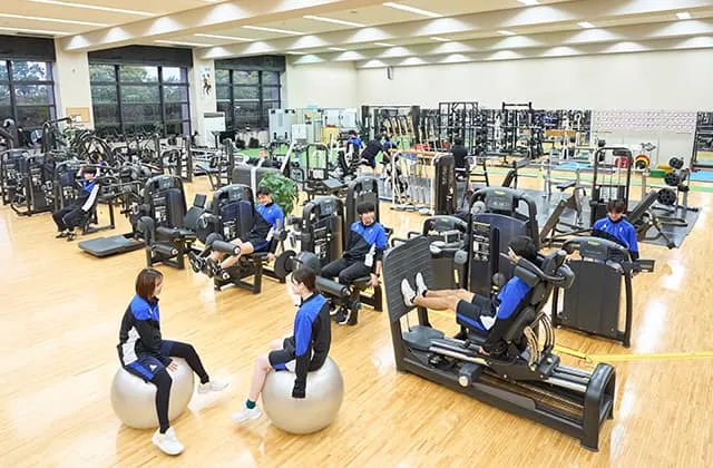 遠くの設備が判別できないくらい広い室内にたくさんのトレーニング器具が並んでいる風景