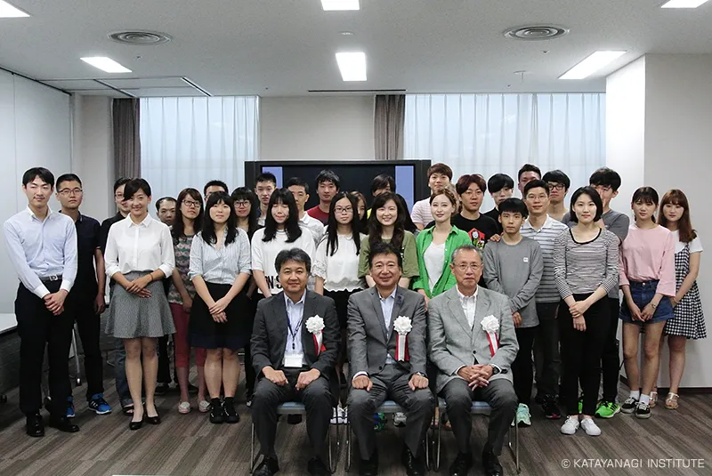 理事長を含む胸章を付けた3人が椅子に座り、新入生たちが後ろに並んでいる様子