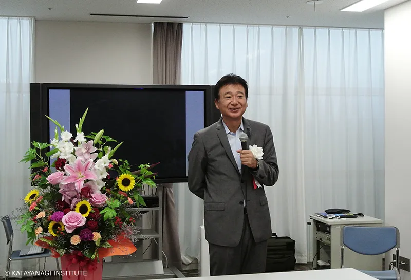 華やかなアレンジメントフラワーの隣に立ち、挨拶をする理事長