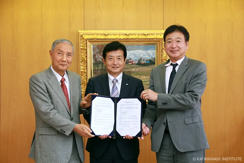 絵画の前で締結書を持ち記念撮影をする3校のトップ