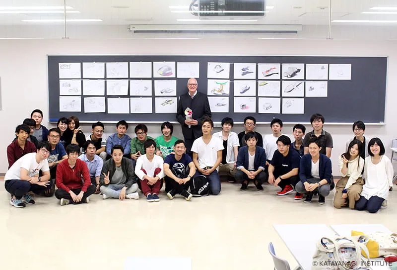 特別講義にて学生たちが制作したデザイン画を掲示した黒板をバックに撮影した、デヴィッド・ロブ氏と学生達の記念写真
