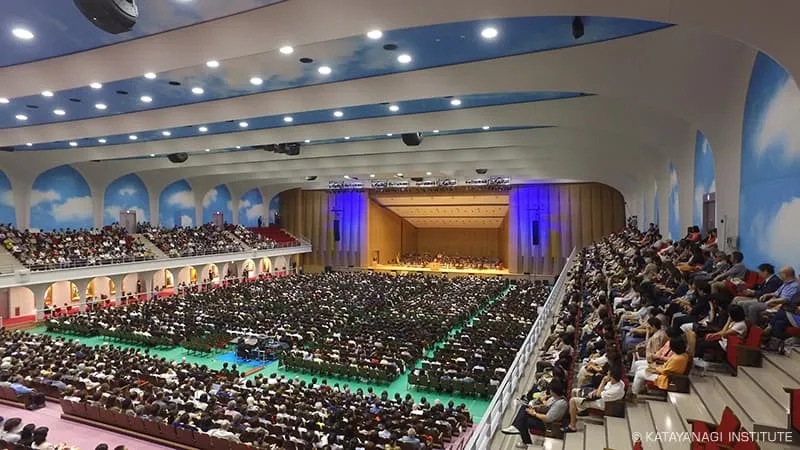 天井と2階の観客席の壁に青空が描かれた館内が、アリーナ席まで満席になっている風景