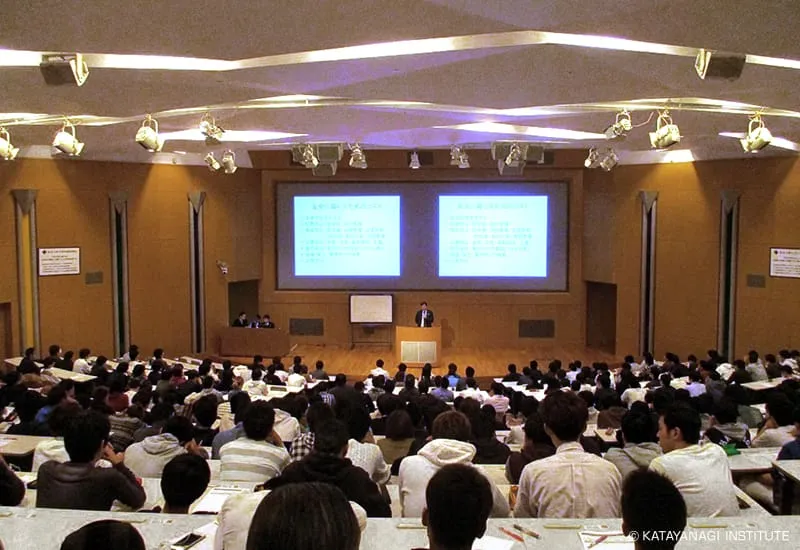 講義中の壇上を階段状の座席の後方から撮影した写真