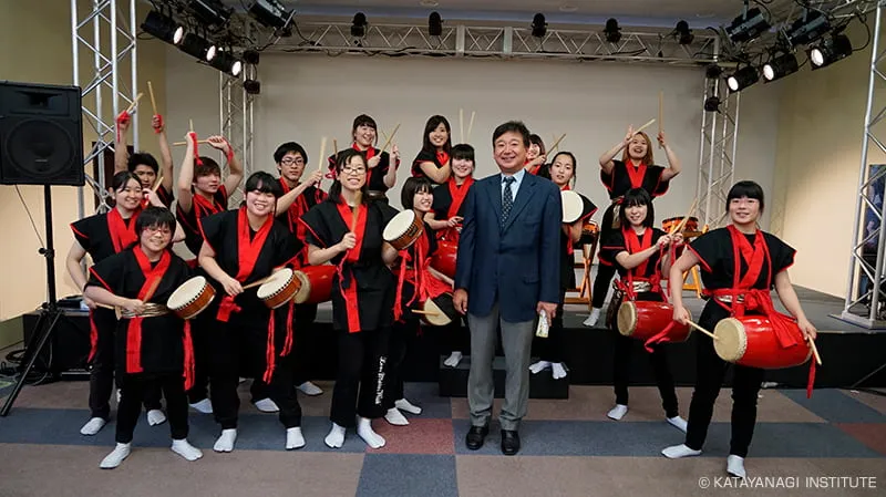 黒に赤の襟と帯の衣装を着てそれぞれ担当の和太鼓と撥を持った学生達と記念撮影