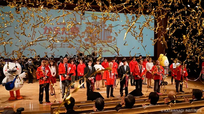 金色のテープが舞っている壇上に赤い法被を着た学校責任者たち、来賓、実行委員会が並び、蒲田キャンパス公式キャラクターかまトゥと東京工科大学公式キャラクターこうかとんの姿も見える開会式の様子