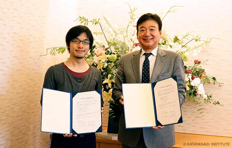 清楚なフラワーアレンジメントの前で社長とならび、それぞれ協定書を手に記念撮影