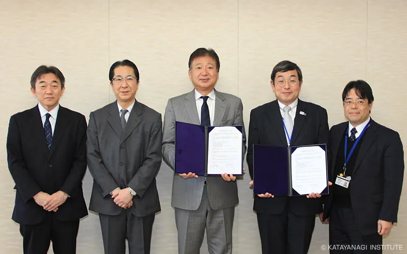 締結書を手に関係者と並んでの記念写真