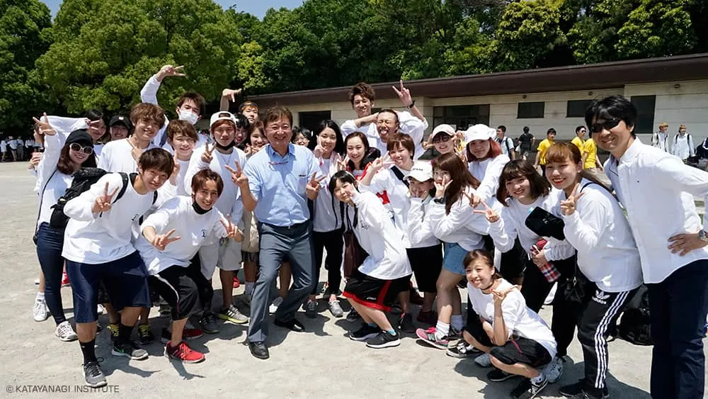 お揃いの白いTシャツを着た学生たちとぎゅっと集まり両手でピースサイン