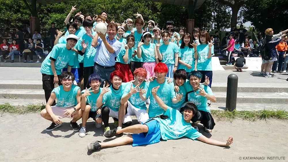 水色のTシャツの学生たちとぎゅっと集まり、校長はボールを持って記念写真