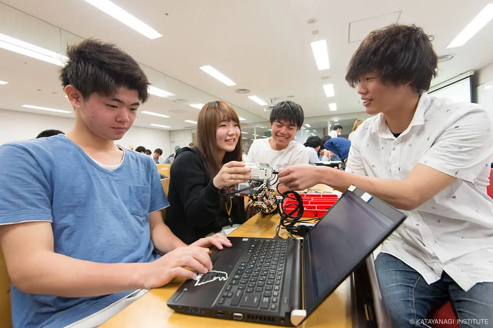 くみ上げた機体にケーブルを接続し支えている、楽しそうな学生たち