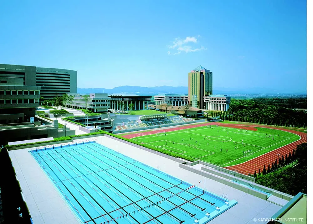 手前に屋外プールと総合グラウンド、奥川に各校舎と片柳研究所棟が見える写真