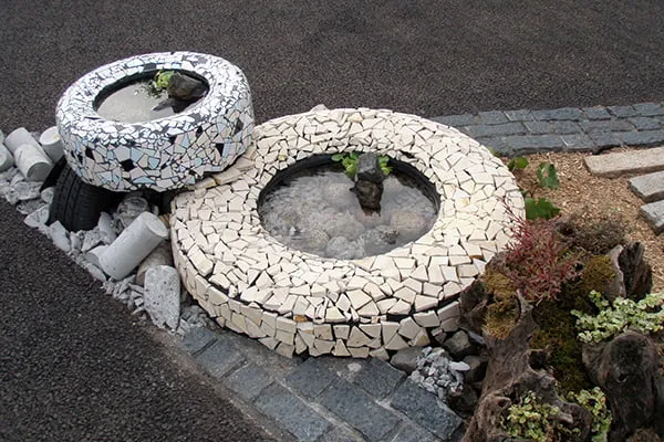 岩をくりぬいて作った水槽を兼ねるオブジェのように見える、モザイク加工がされた古タイヤ2つ