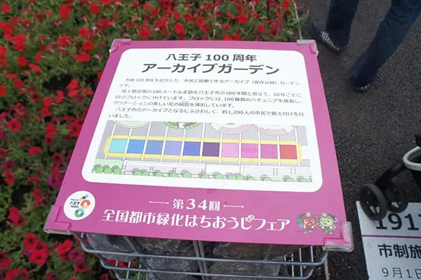 市制100周年を記念した、市民と共同で作るアーカイブガーデンについて解説したプレート。元は陸上競技場の100メートル走路だった場所を八王子市の100年間に見立て、10年ごとに10のブロック、100種類のペチュニアを植栽し、グラデーションの美しい花の絨毯を演出している。