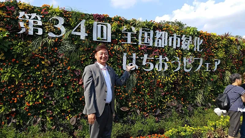 フェアのサインが掲示された草花で作られた壁面の前で記念撮影をする校長