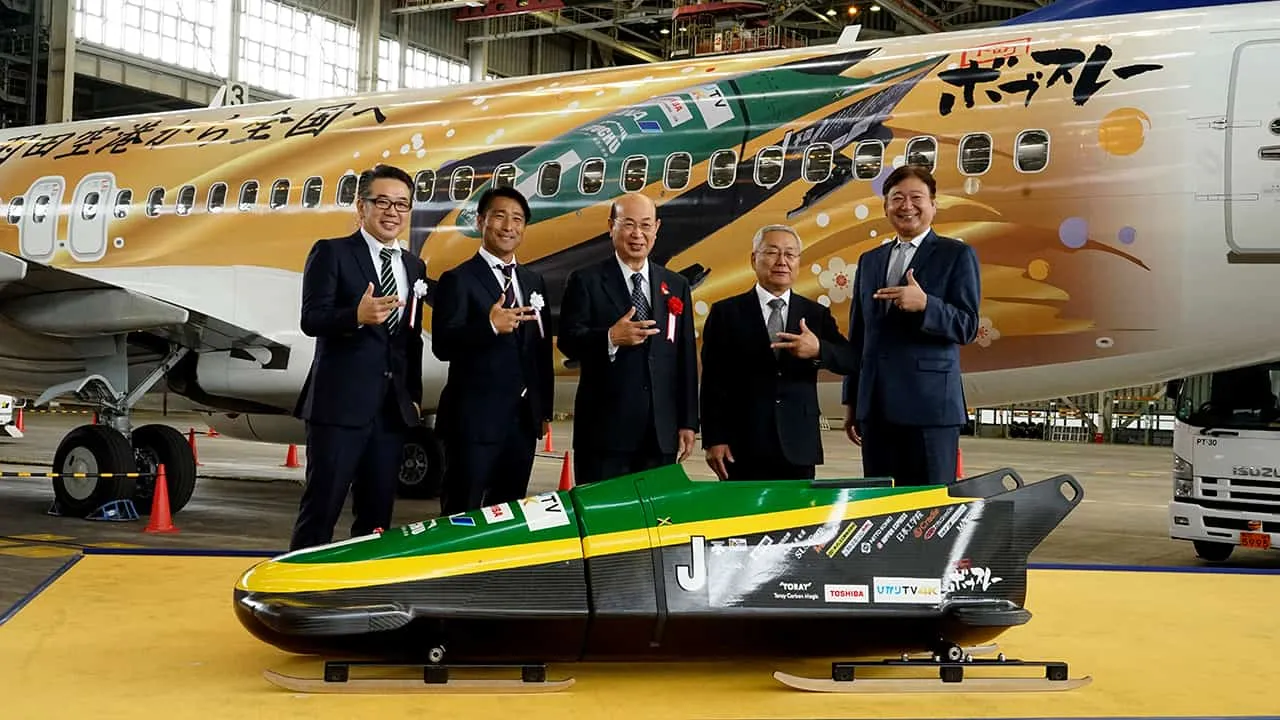 ボブスレーとジェット機の間に立ち、お揃いのポーズで楽しそうに記念撮影