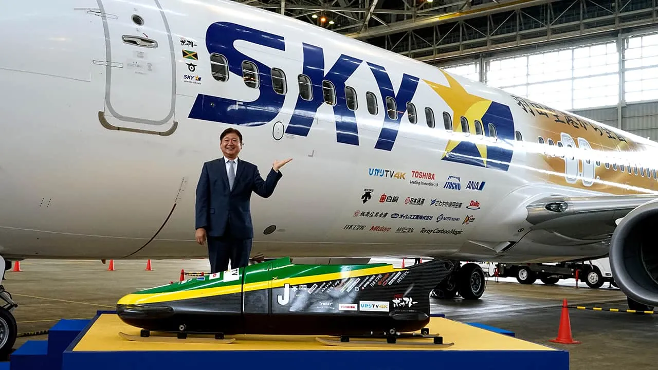 手前にボブスレーの機体、後ろにジェット機の機体の立ち位置で笑顔の機縁撮影